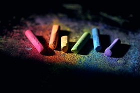 six sticks of chalk in different colors on dark surface